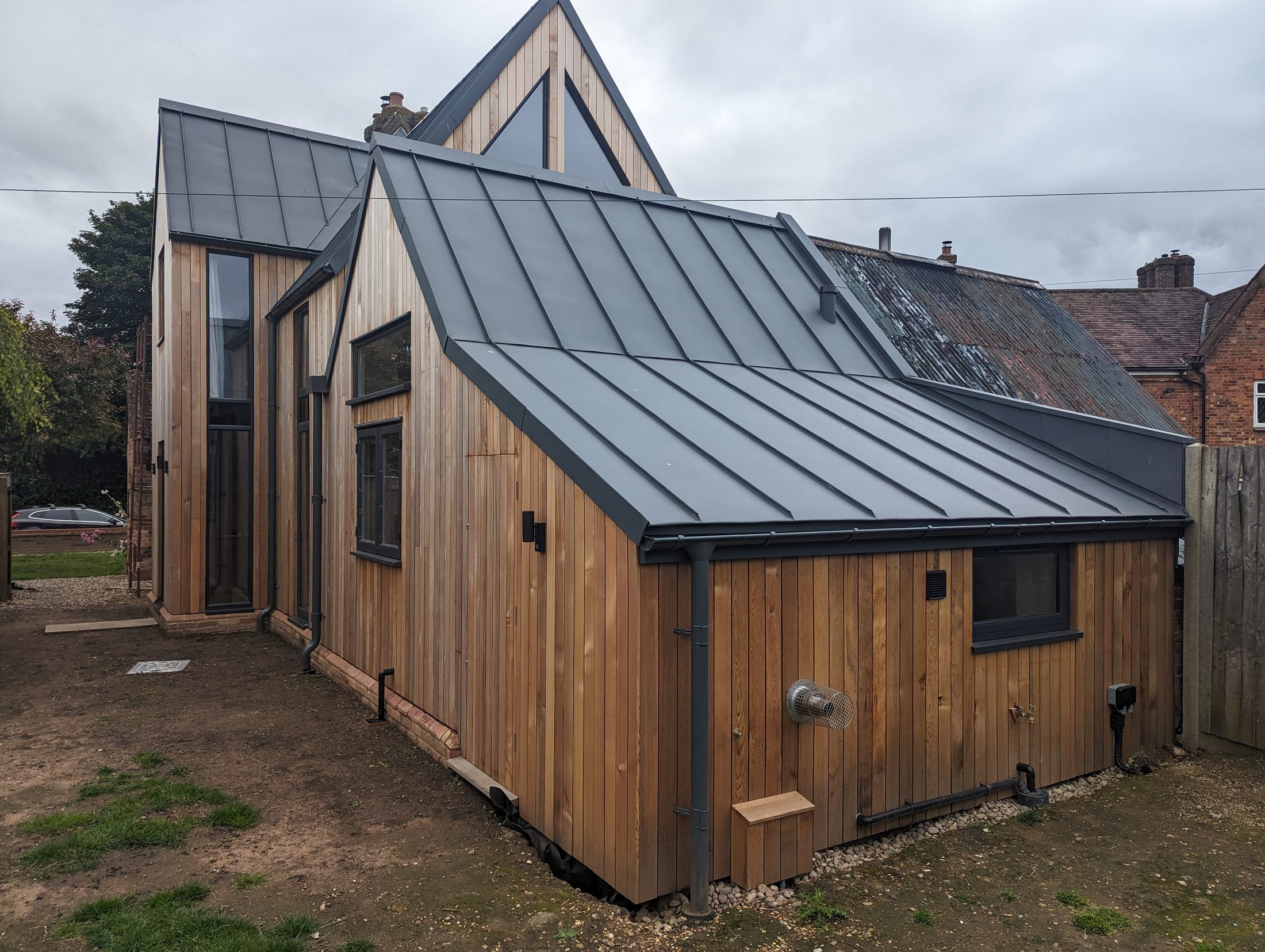 Finished standing-seam metal roof on a timber-clad home extension.
